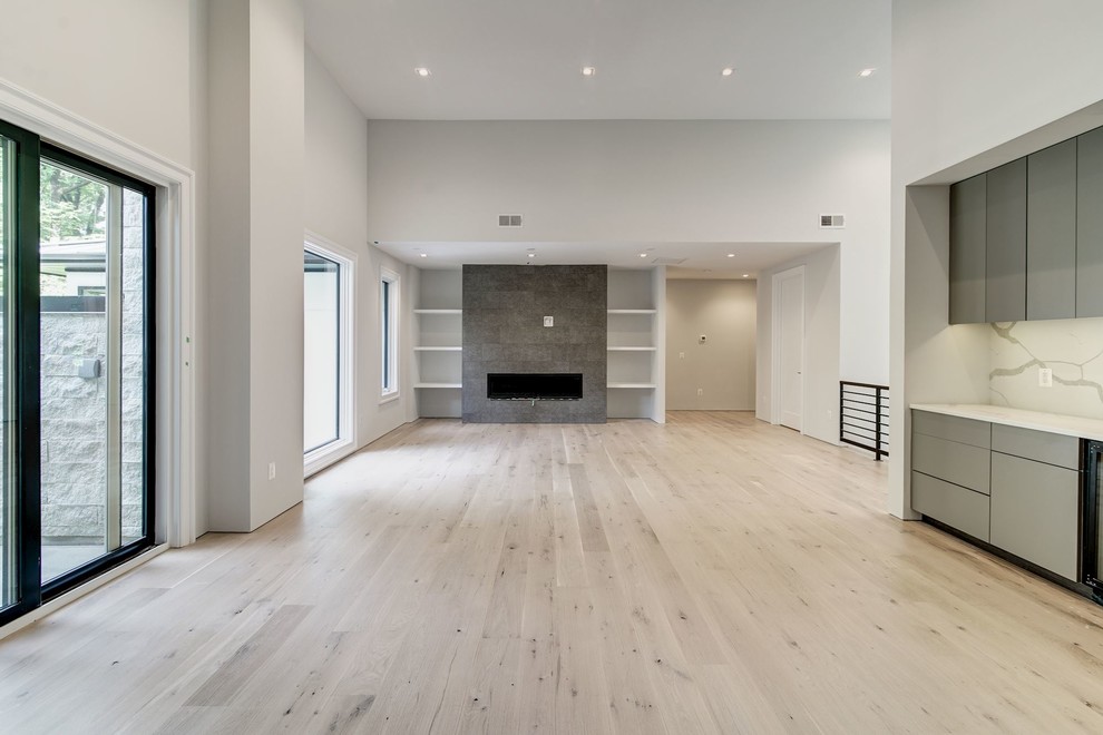 Photo of a large modern open plan living room in DC Metro with a home bar, white walls, light hardwood flooring, a ribbon fireplace, a tiled fireplace surround, no tv and beige floors.