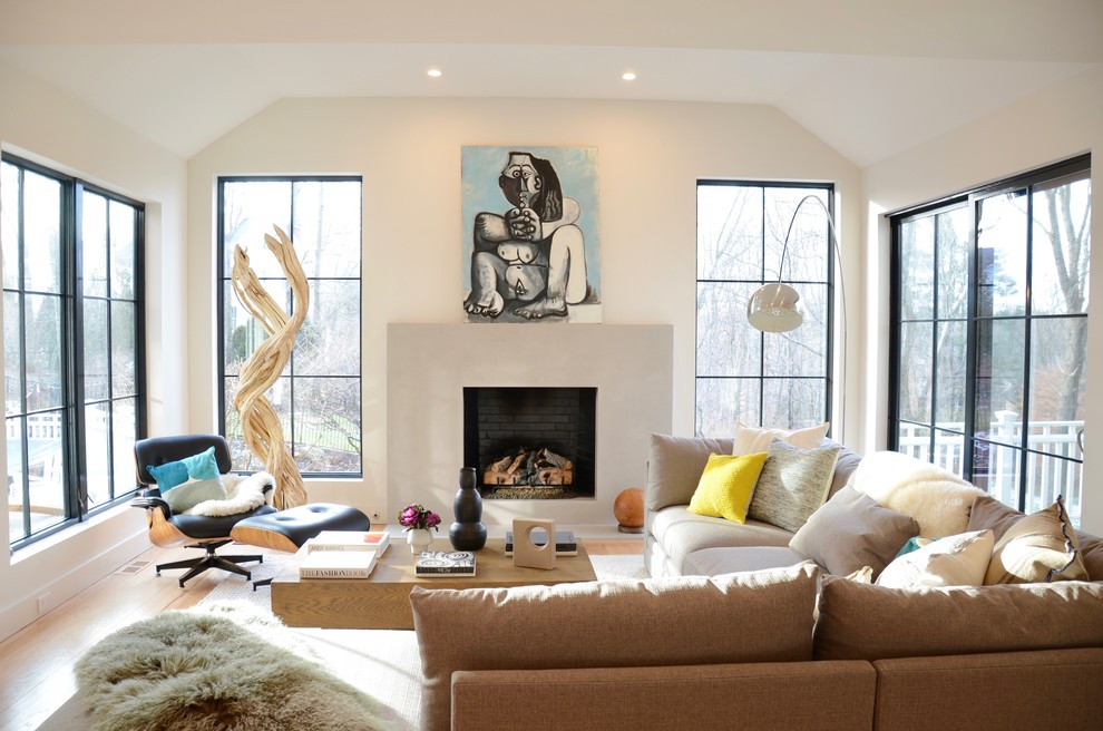 Example of a large minimalist open concept light wood floor and beige floor living room design in New York with gray walls, a standard fireplace and a concrete fireplace
