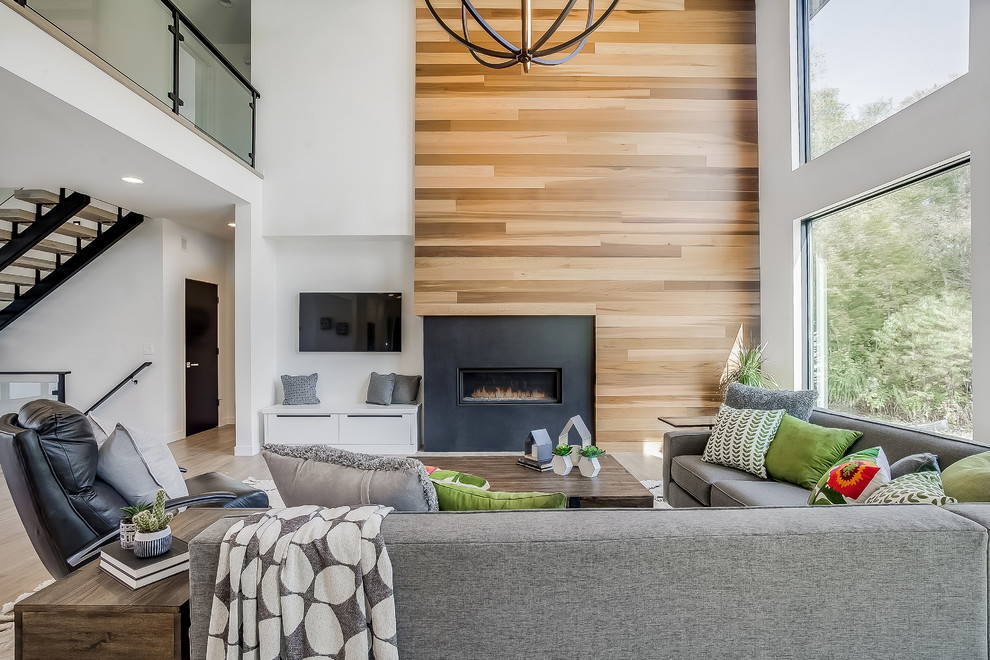 This is an example of an expansive contemporary open plan living room in Grand Rapids with white walls, a standard fireplace, a wooden fireplace surround and a wall mounted tv.