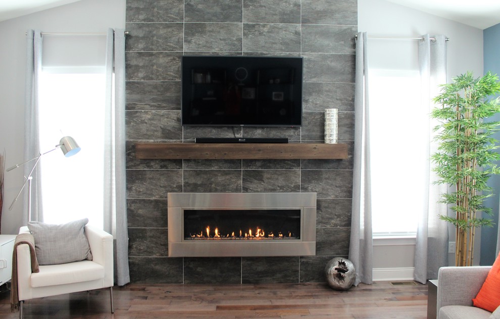 Ejemplo de salón minimalista grande con paredes grises, suelo de madera en tonos medios, chimenea lineal, marco de chimenea de piedra y televisor colgado en la pared