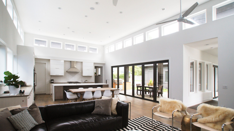 Imagen de salón abierto moderno grande con paredes blancas, suelo de madera en tonos medios, chimenea lineal, marco de chimenea de yeso y televisor colgado en la pared