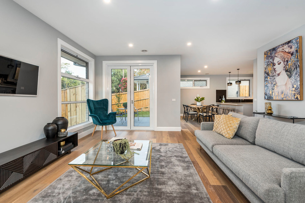 Großes, Offenes Modernes Wohnzimmer mit grauer Wandfarbe, TV-Wand, braunem Holzboden und braunem Boden in Melbourne