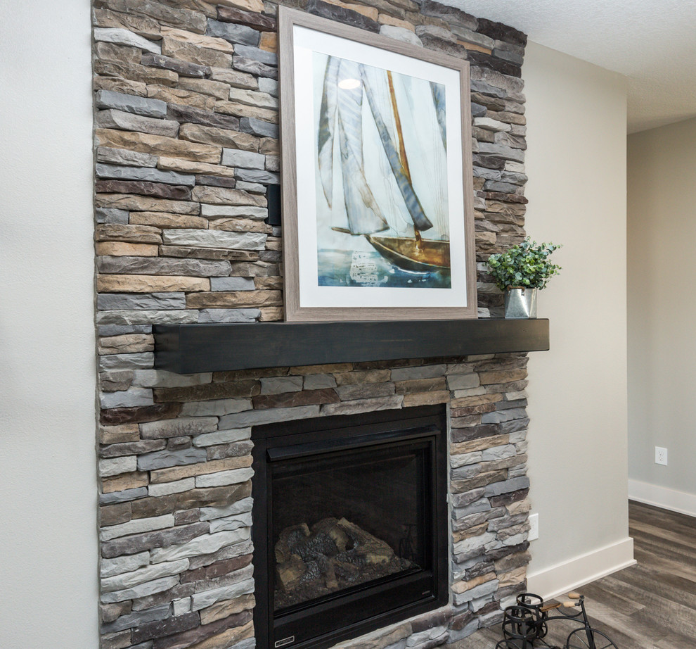 Cette photo montre un salon moderne ouvert avec un mur gris, un sol en vinyl, une cheminée standard, un manteau de cheminée en pierre, un téléviseur fixé au mur et un sol gris.