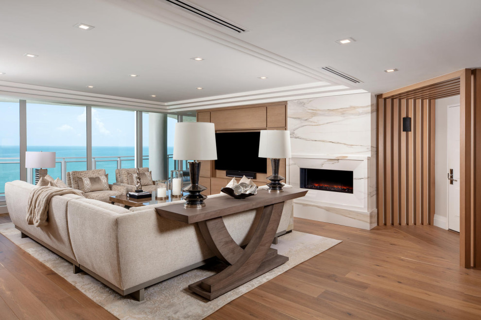 マイアミにあるラグジュアリーな広いビーチスタイルのおしゃれなLDK (白い壁、無垢フローリング、標準型暖炉、石材の暖炉まわり、埋込式メディアウォール、茶色い床) の写真