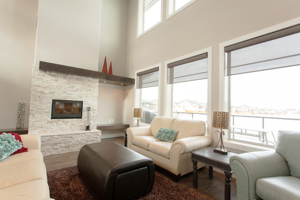 Immagine di un grande soggiorno minimalista aperto con pareti beige, pavimento in legno massello medio, camino classico e cornice del camino in pietra
