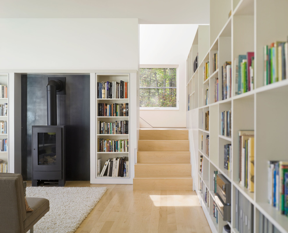 Diseño de biblioteca en casa campestre con suelo de madera clara, estufa de leña y alfombra