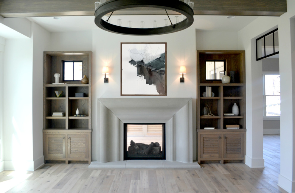 Modelo de salón para visitas abierto campestre grande con paredes blancas, suelo de madera clara, chimenea de doble cara, marco de chimenea de hormigón y televisor colgado en la pared
