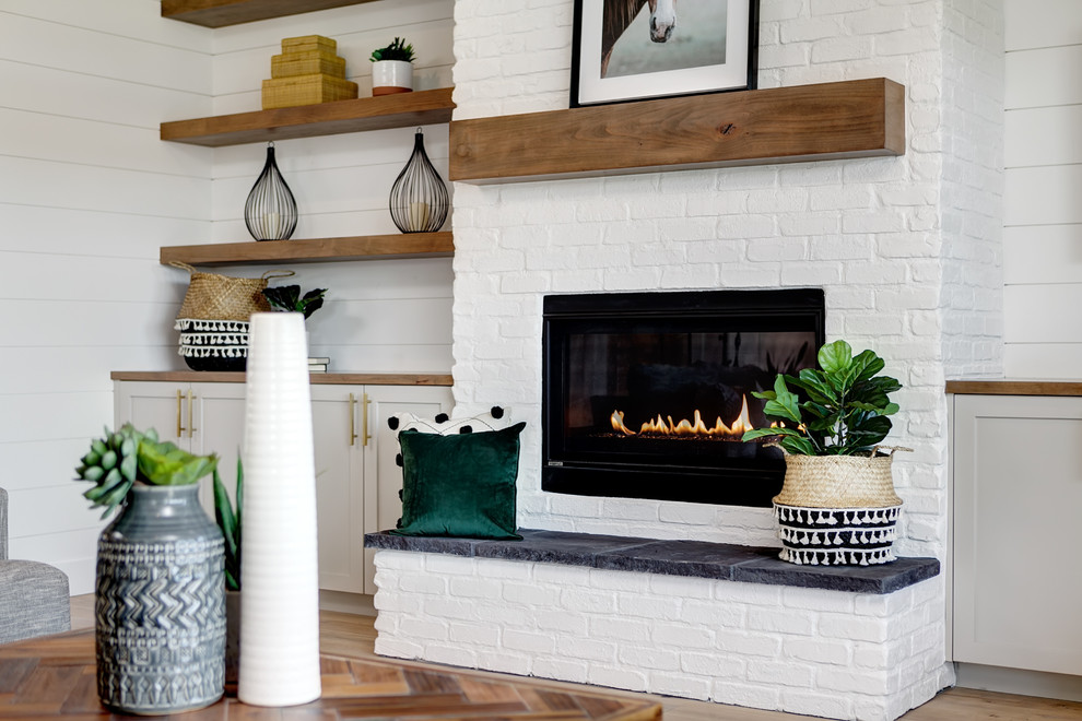 ボイシにある広いカントリー風のおしゃれなLDK (白い壁、淡色無垢フローリング、標準型暖炉、レンガの暖炉まわり、壁掛け型テレビ、ベージュの床) の写真