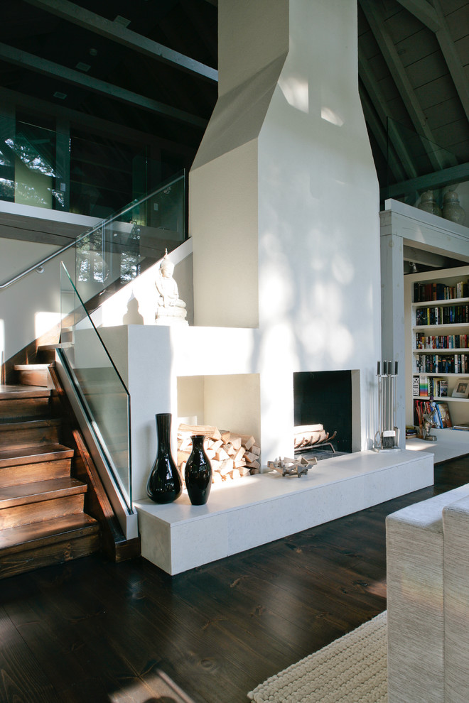 Cette photo montre un salon nature de taille moyenne avec une bibliothèque ou un coin lecture, parquet foncé, un mur gris, aucun téléviseur, une cheminée double-face et un escalier.