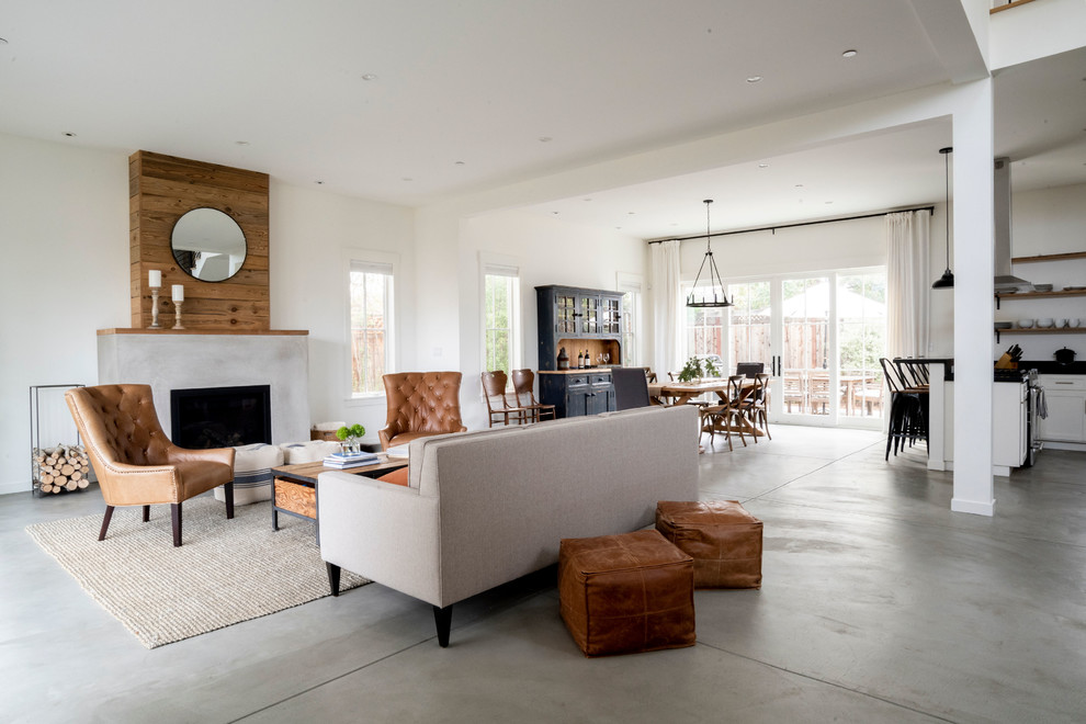 Diseño de salón abierto campestre de tamaño medio con paredes blancas, suelo de cemento, marco de chimenea de madera y suelo gris