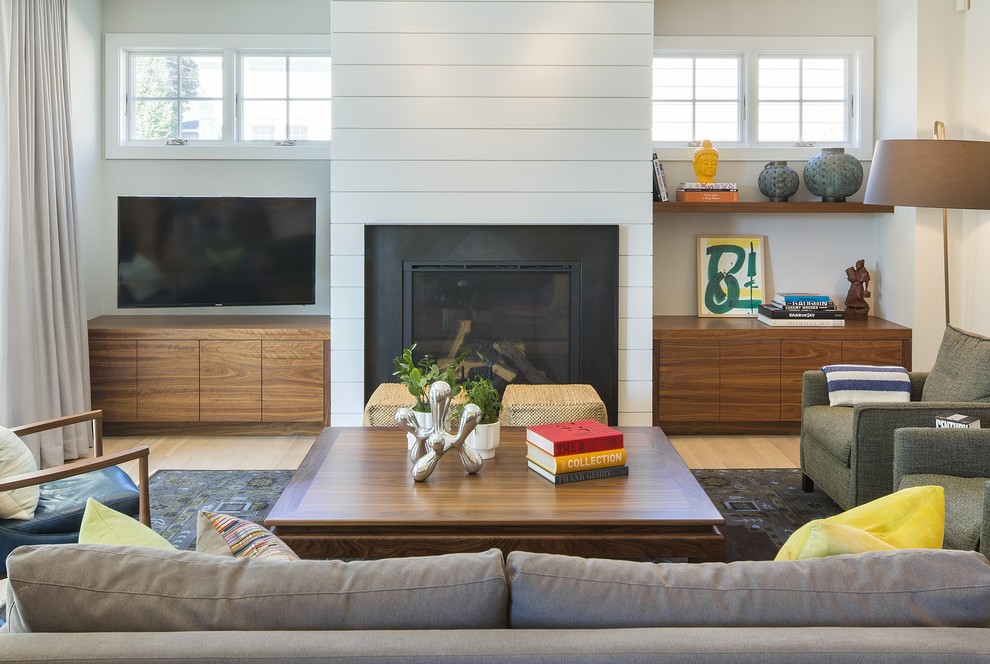 Foto de salón abierto minimalista de tamaño medio con paredes blancas, suelo de madera clara, todas las chimeneas, marco de chimenea de metal y televisor colgado en la pared