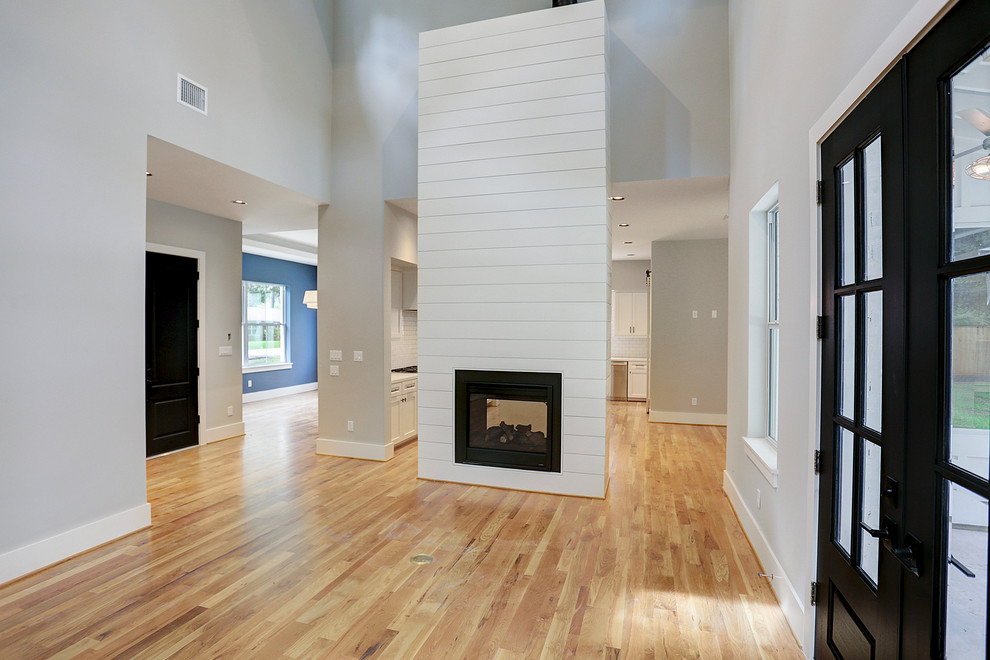 На фото: большая открытая гостиная комната в стиле кантри с серыми стенами, светлым паркетным полом, двусторонним камином, фасадом камина из дерева и бежевым полом с
