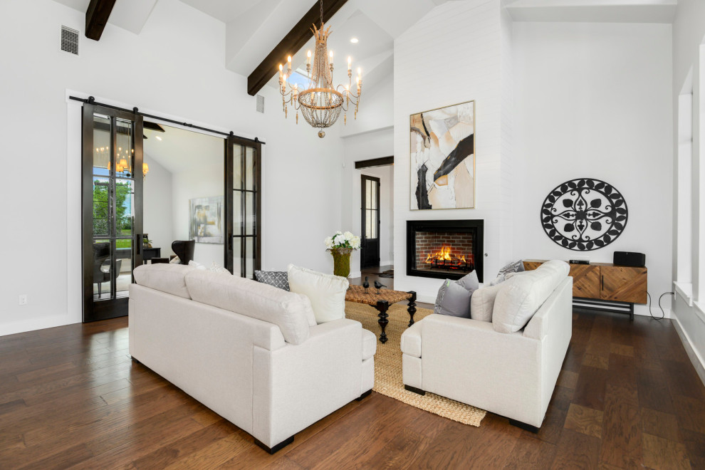 This is an example of a medium sized rural formal open plan living room in Austin with white walls, dark hardwood flooring, a hanging fireplace, a metal fireplace surround, no tv, brown floors and a vaulted ceiling.