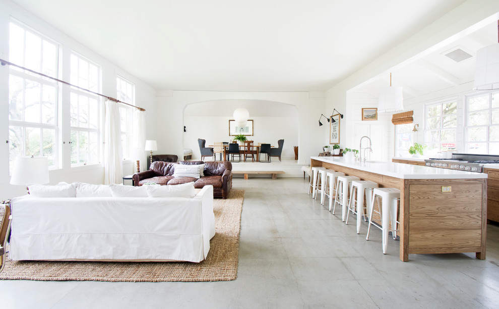 Réalisation d'un grand salon champêtre ouvert avec un mur blanc, un sol gris et sol en béton ciré.