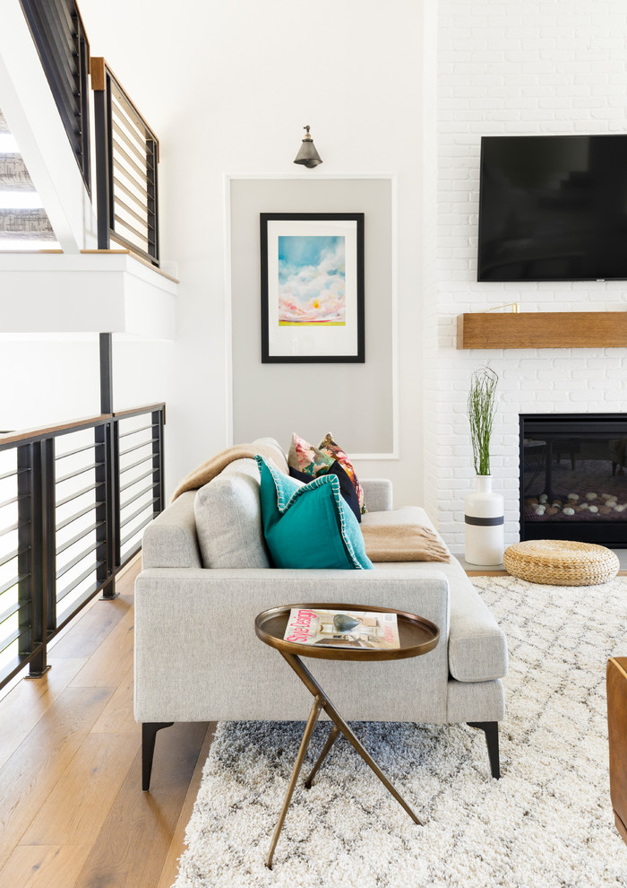 Свежая идея для дизайна: открытая гостиная комната в стиле неоклассика (современная классика) с белыми стенами, светлым паркетным полом, стандартным камином, фасадом камина из кирпича, телевизором на стене и коричневым полом - отличное фото интерьера