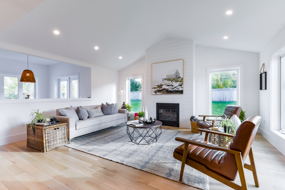 Large country open plan living room in Toronto with white walls, light hardwood flooring, a standard fireplace, a timber clad chimney breast, brown floors and a vaulted ceiling.