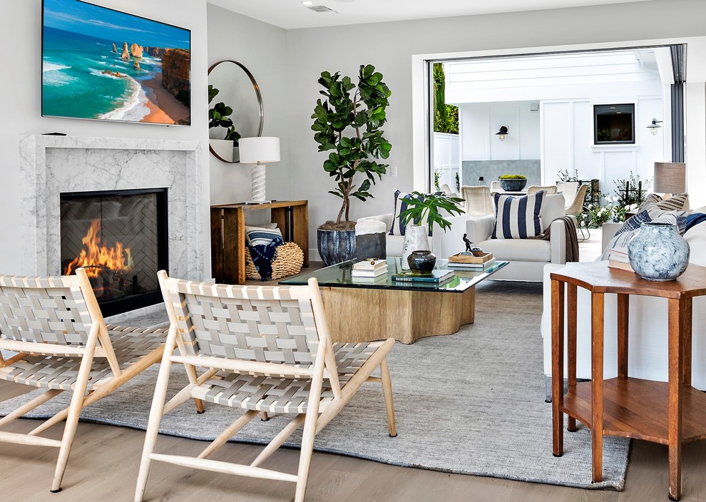 Beach style open concept medium tone wood floor and beige floor living room photo in Orange County with white walls, a standard fireplace, a stone fireplace and a wall-mounted tv