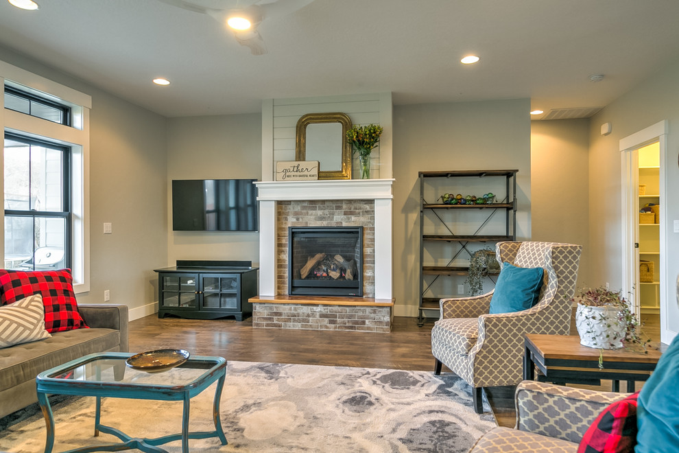 Inspiration for a large country open plan living room in Boise with grey walls, laminate floors, a standard fireplace, a brick fireplace surround, a wall mounted tv and brown floors.