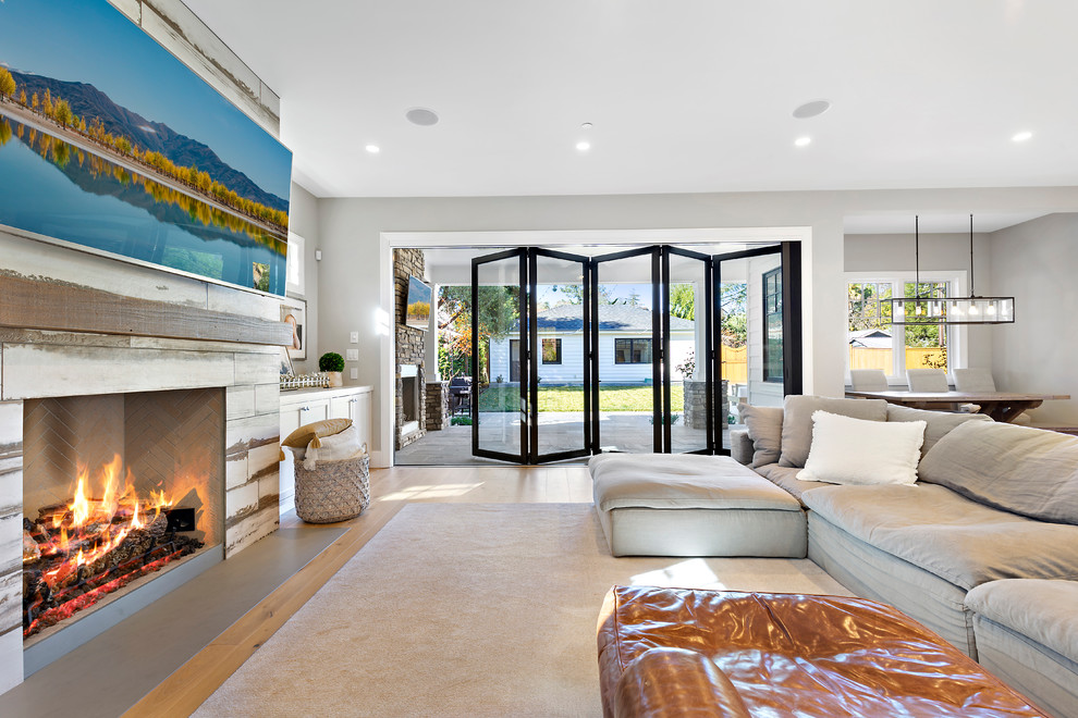 Geräumiges, Offenes Landhausstil Wohnzimmer mit grauer Wandfarbe, hellem Holzboden, Kaminumrandung aus Holz und TV-Wand in Los Angeles