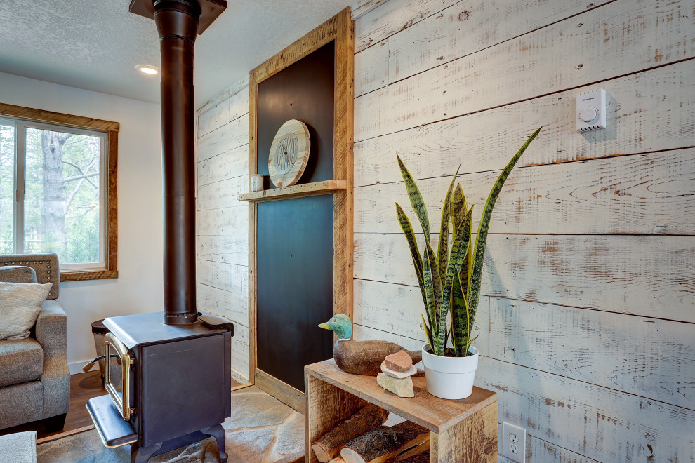 Immagine di un soggiorno rustico di medie dimensioni e aperto con pareti bianche, pavimento in laminato, stufa a legna, cornice del camino in pietra e pavimento marrone