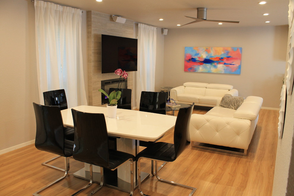 Imagen de salón abierto moderno grande con paredes grises, suelo de madera clara, marco de chimenea de baldosas y/o azulejos y televisor colgado en la pared