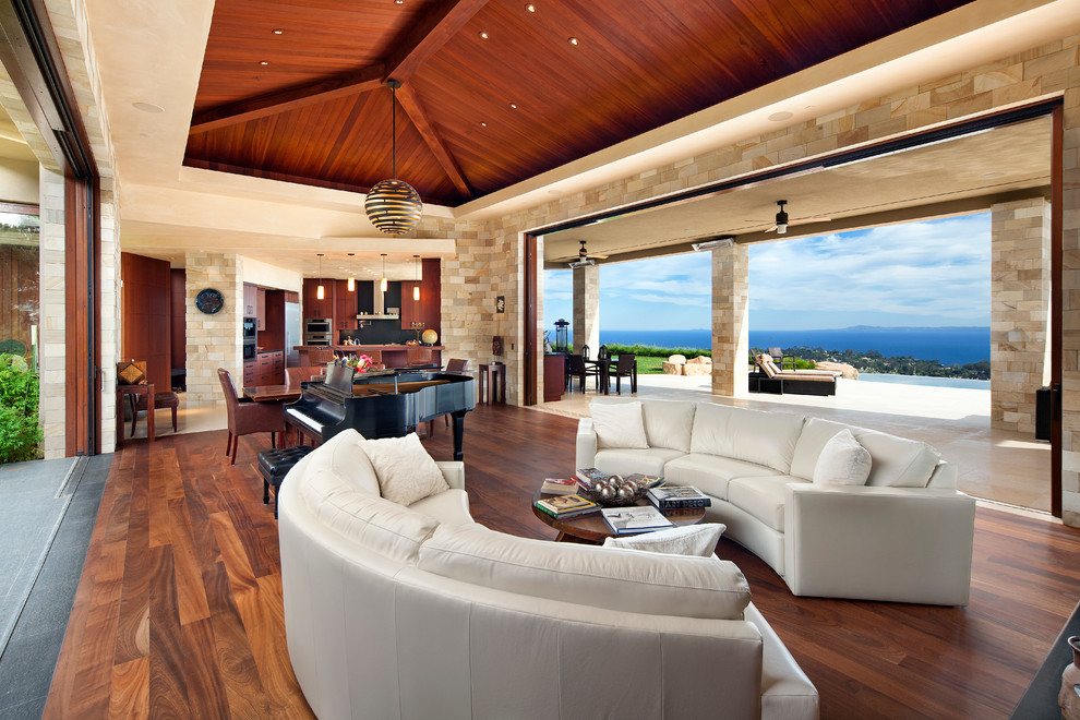 Photo of an expansive world-inspired open plan living room in Santa Barbara with beige walls, dark hardwood flooring, a two-sided fireplace, a stone fireplace surround and no tv.