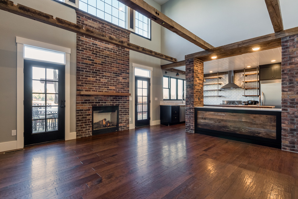 Cette photo montre un grand salon industriel ouvert avec une salle de réception, un mur gris, un sol en bois brun, une cheminée standard, un manteau de cheminée en brique et aucun téléviseur.