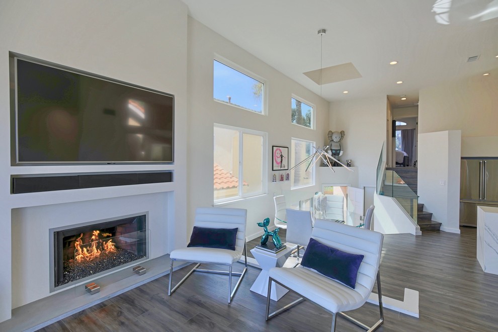 Mittelgroßes, Offenes Modernes Wohnzimmer mit weißer Wandfarbe, Laminat, Kamin, Kaminumrandung aus Beton, Multimediawand und grauem Boden in Orange County