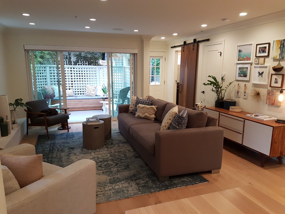 Small modern open plan living room in Vancouver with white walls, light hardwood flooring, a standard fireplace, a wooden fireplace surround and a wall mounted tv.