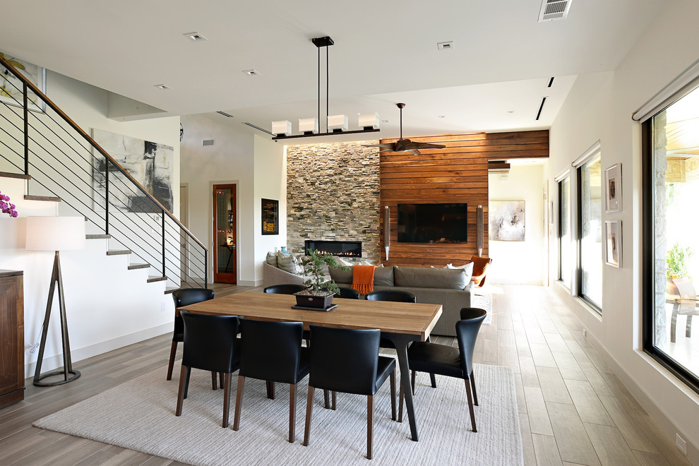 Cette image montre une salle à manger minimaliste de taille moyenne avec un mur blanc, un sol en bois brun, une cheminée standard, un manteau de cheminée en pierre et un sol gris.