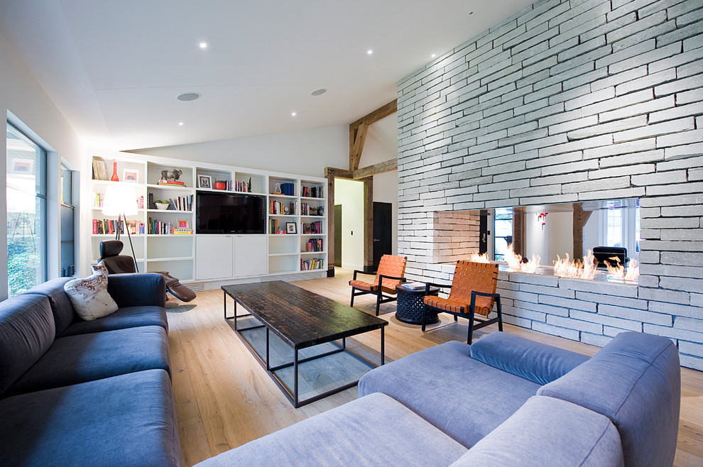 Esempio di un soggiorno minimalista con libreria, camino bifacciale e parete attrezzata