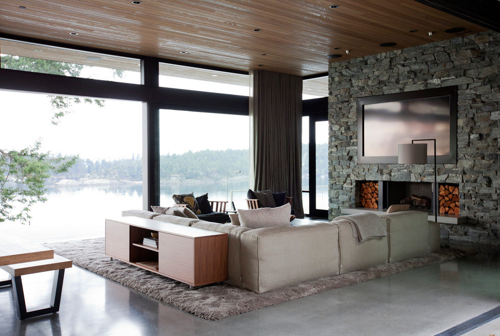 Cette image montre un grand salon minimaliste ouvert avec sol en béton ciré, une cheminée standard, un manteau de cheminée en pierre et un téléviseur fixé au mur.