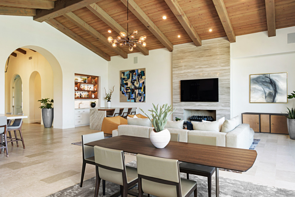 サンディエゴにあるラグジュアリーな広い地中海スタイルのおしゃれなリビング (白い壁、ライムストーンの床、標準型暖炉、石材の暖炉まわり、壁掛け型テレビ、ベージュの床) の写真