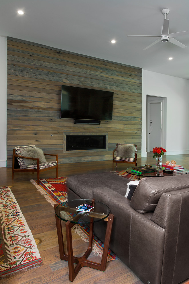 На фото: большая открытая гостиная комната в стиле модернизм с белыми стенами, паркетным полом среднего тона, стандартным камином, фасадом камина из дерева, телевизором на стене и коричневым полом с