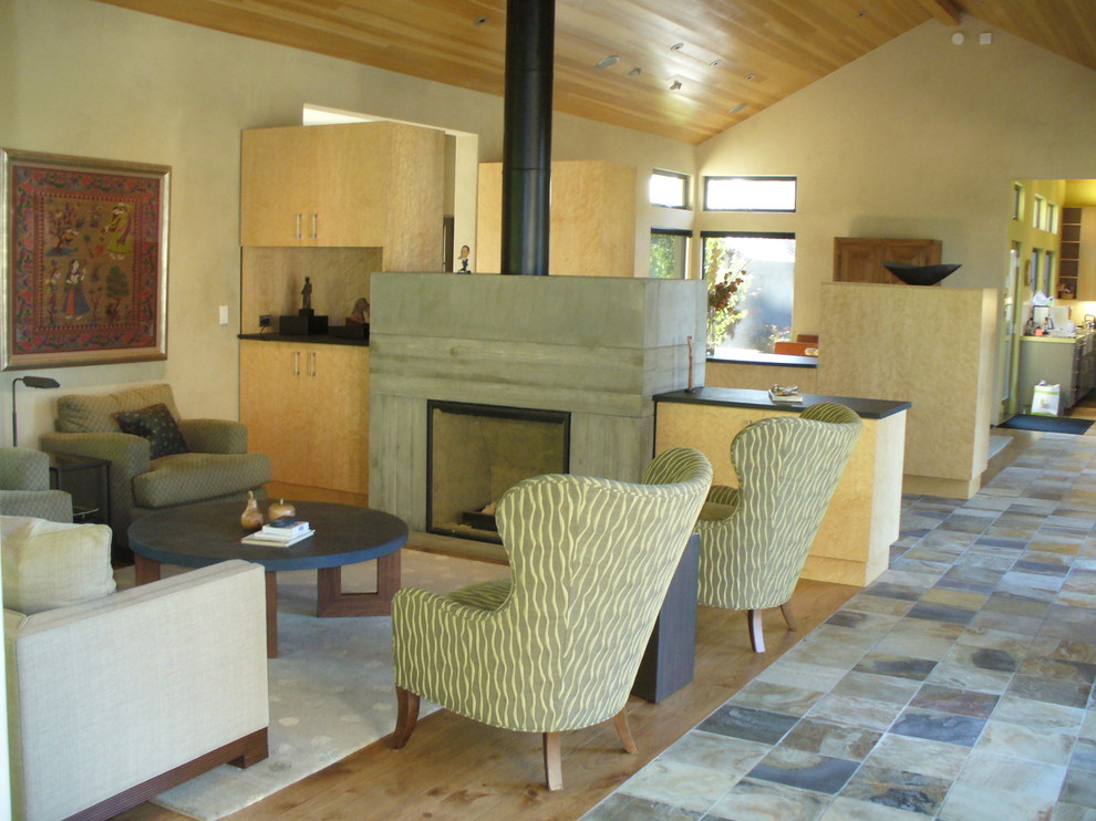 Foto de salón para visitas abierto actual de tamaño medio con paredes beige, suelo de madera clara, estufa de leña y marco de chimenea de hormigón