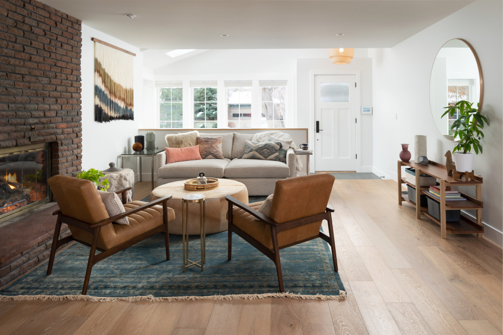Esempio di un soggiorno minimalista aperto con pareti bianche, parquet chiaro, stufa a legna e cornice del camino in mattoni