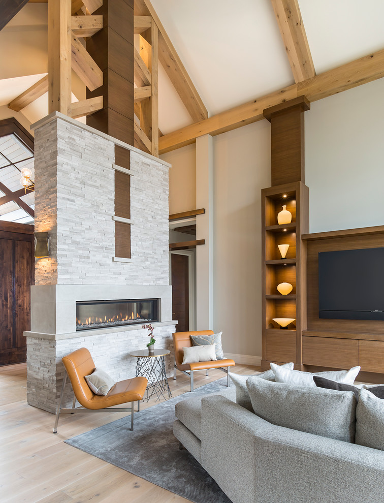 Cette image montre un très grand salon design ouvert avec un mur gris, parquet clair, une cheminée double-face, un manteau de cheminée en pierre et un téléviseur encastré.