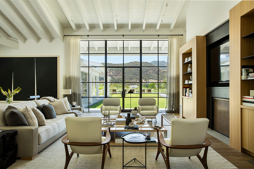 Immagine di un soggiorno country con pareti bianche, pavimento in legno massello medio, camino classico, TV a parete e pavimento marrone