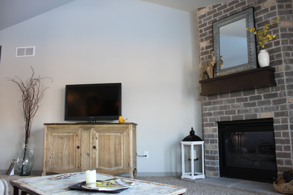 Imagen de salón abierto de estilo americano de tamaño medio con paredes grises, moqueta, chimenea de esquina, marco de chimenea de ladrillo y televisor independiente