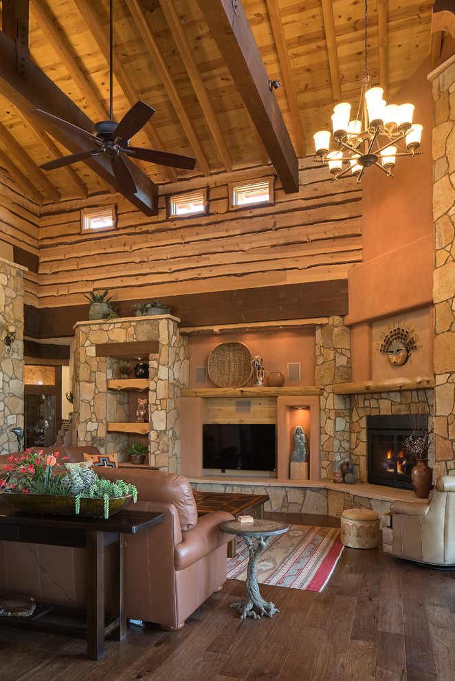 フェニックスにある高級な広いサンタフェスタイルのおしゃれなリビング (オレンジの壁、淡色無垢フローリング、石材の暖炉まわり、壁掛け型テレビ、標準型暖炉) の写真