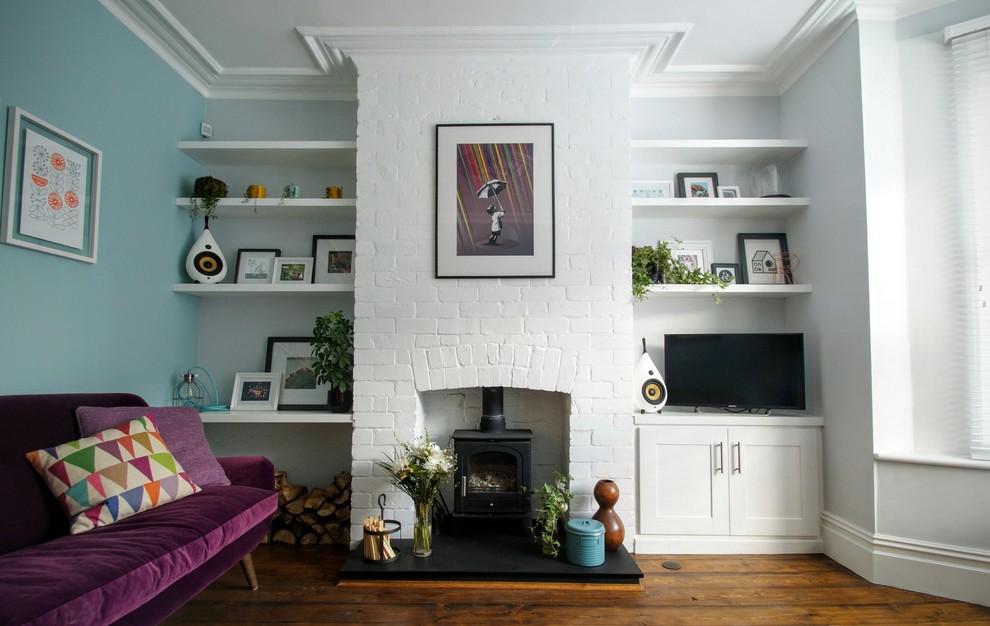 Ejemplo de salón cerrado moderno de tamaño medio con paredes azules, suelo de madera en tonos medios, estufa de leña y marco de chimenea de ladrillo