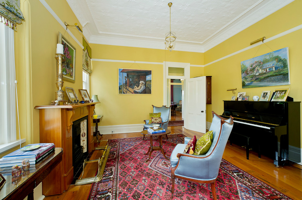 Foto de salón con rincón musical cerrado tradicional de tamaño medio con paredes amarillas, todas las chimeneas, marco de chimenea de madera y suelo marrón
