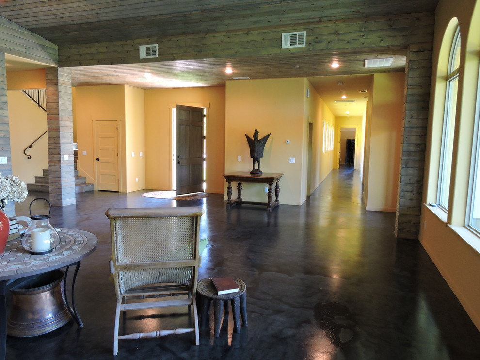 Modelo de salón para visitas abierto rústico grande sin chimenea y televisor con paredes amarillas, suelo de cemento y suelo negro