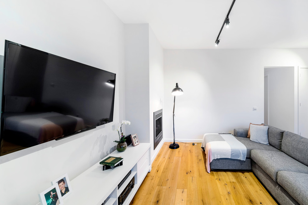Ejemplo de salón abierto moderno de tamaño medio con paredes blancas, suelo de madera en tonos medios, chimeneas suspendidas y televisor colgado en la pared