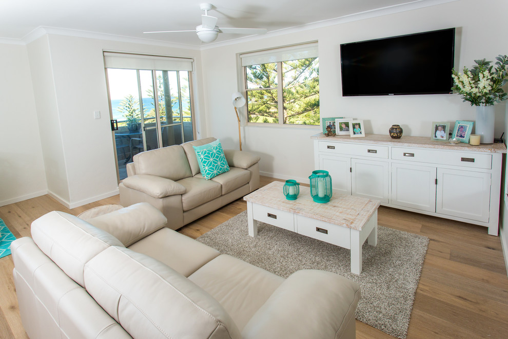 Foto de salón abierto costero con paredes blancas, suelo de madera clara y televisor colgado en la pared