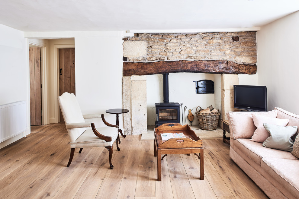 Cette photo montre un salon nature de taille moyenne et fermé avec un mur blanc, un sol en bois brun, un poêle à bois, un manteau de cheminée en pierre, un téléviseur indépendant et un sol marron.