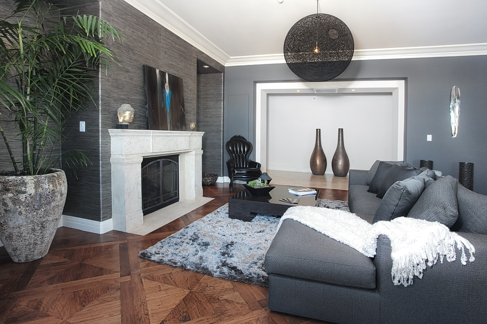 Cette image montre un grand salon design ouvert avec une salle de réception, un mur gris, un sol en bois brun, une cheminée standard, un manteau de cheminée en pierre et aucun téléviseur.