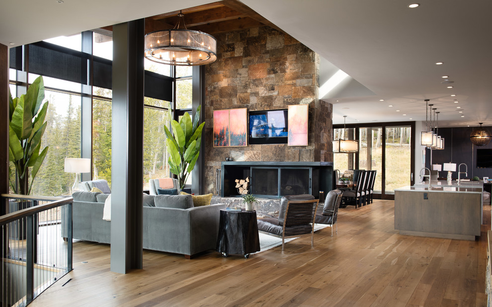 Foto de salón abierto rústico con suelo de madera en tonos medios, todas las chimeneas, marco de chimenea de piedra, suelo marrón y televisor retractable