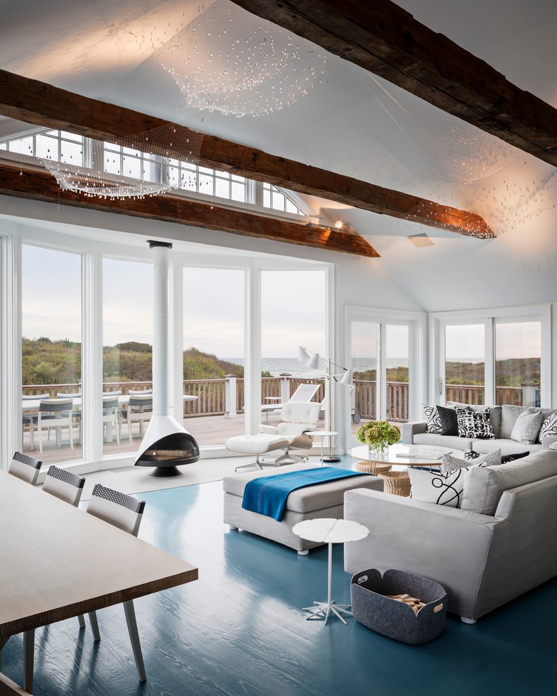 На фото: большая открытая, парадная гостиная комната в морском стиле с белыми стенами, подвесным камином, деревянным полом, фасадом камина из металла и синим полом без телевизора
