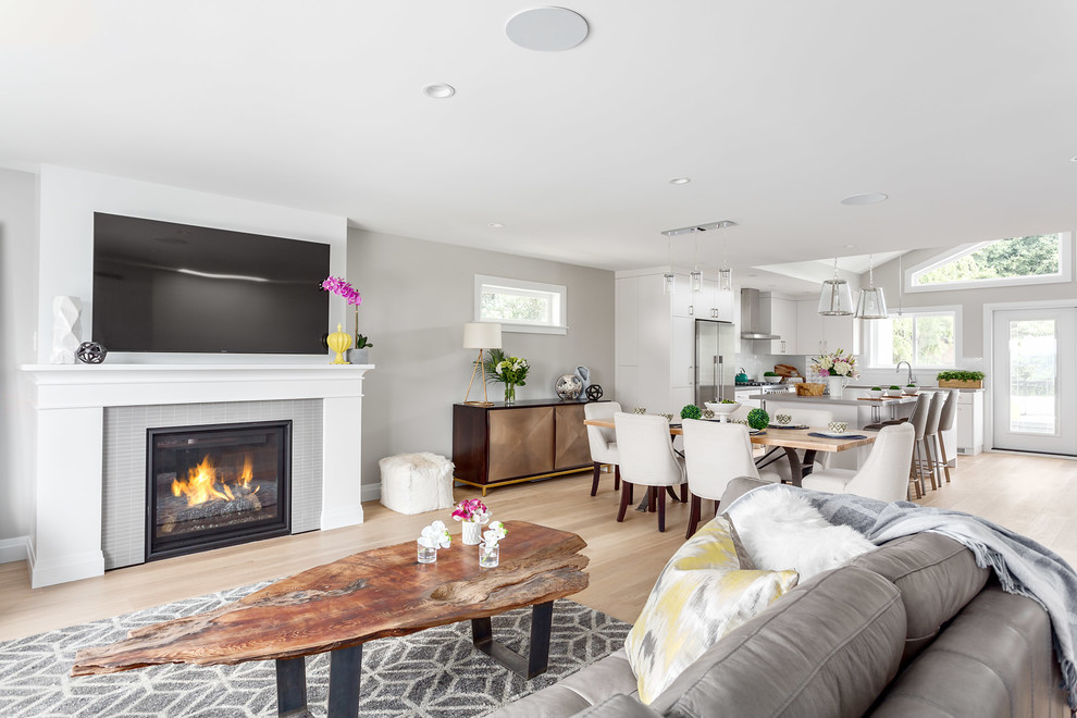 This is an example of a medium sized contemporary open plan living room in Vancouver with grey walls, light hardwood flooring, a standard fireplace, a tiled fireplace surround, a wall mounted tv and brown floors.